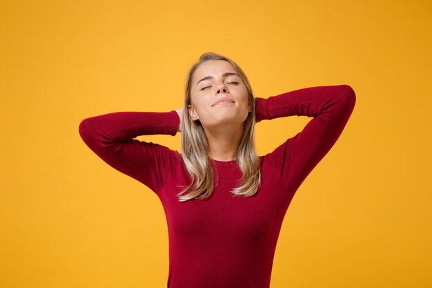 Una joven rubia relajada con ropa informal posando aislada en un retrato de estudio de fondo de pared naranja amarillo. Concepto de estilo de vida de las emociones de las personas. Simulacros de espacio de copia. Dormir con las manos detrás de la cabeza.