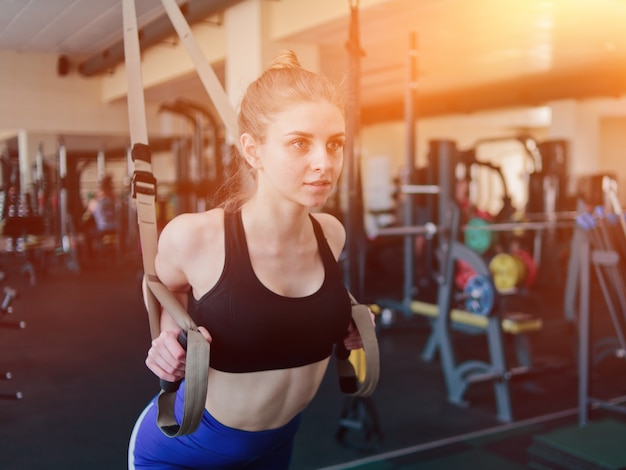 Joven rubia en ropa deportiva haciendo ejercicio con correas de fitness en el gimnasio. Entrenamiento funcional