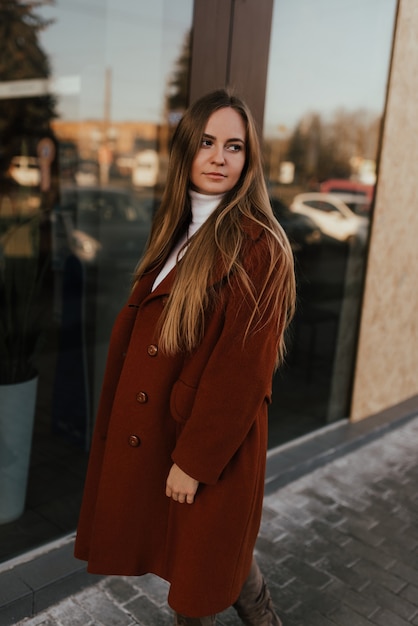 Joven rubia en ropa de otoño camina sobre escaparates de fondo de calle.