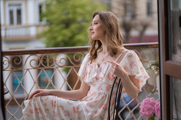 Joven rubia sentada en el balcón con un vestido floral brillante