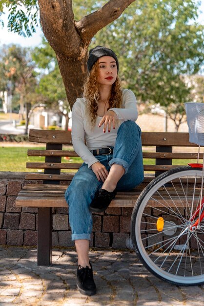 Joven rubia sentada en un banco, descansando en el parque con su bicicleta