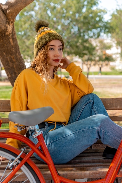 Joven rubia sentada en un banco, descansando en el parque con su bicicleta