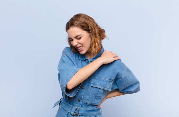 Foto joven rubia se siente cansada, estresada, ansiosa, frustrada y deprimida, sufriendo dolor de espalda o cuello contra la pared de color plano