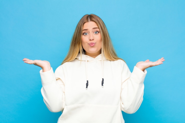 Foto joven rubia se siente confundida y confundida, dudando, ponderando o eligiendo diferentes opciones con expresión divertida contra la pared plana