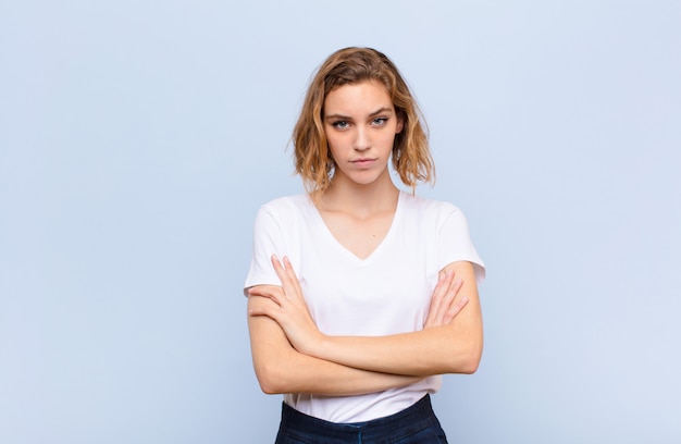 Joven rubia se siente disgustada y decepcionada, se ve seria, molesta y enojada con los brazos cruzados contra la pared de color plano