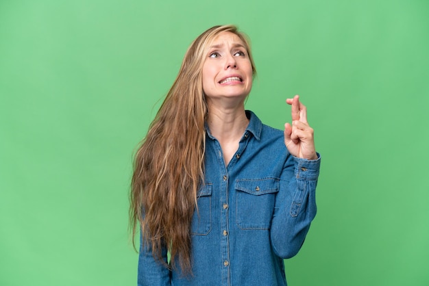 Joven rubia sobre un fondo aislado con los dedos cruzados y deseando lo mejor