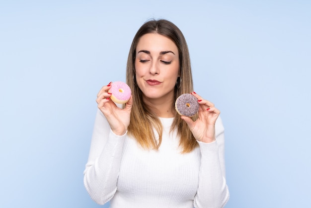 Joven rubia sobre pared azul aislada con donas