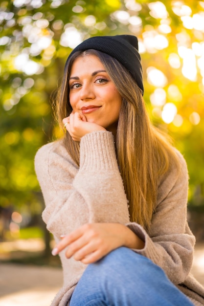 Joven rubia con un sombrero de lana en otoño sentada al atardecer