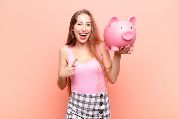 Joven rubia sonriendo alegremente sosteniendo una alcancía