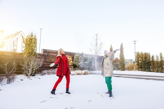 Una joven rubia sonriente y alegre y su alegre madre arrojando nieve al aire