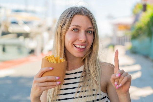 Foto joven rubia sosteniendo papas fritas al aire libre señalando una gran idea