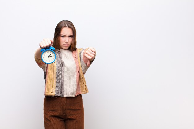 Foto joven rubia sosteniendo un reloj despertador contra la pared blanca