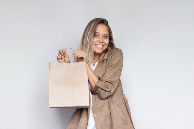 Una joven rubia sostiene y demuestra una bolsa ecológica de papel con copia espacio vacío para el logotipo