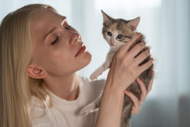 Foto una joven rubia sostiene un pequeño gatito en sus brazos frente a su cara y mira a la mascota con amor. la alegría que traen los animales a la casa.