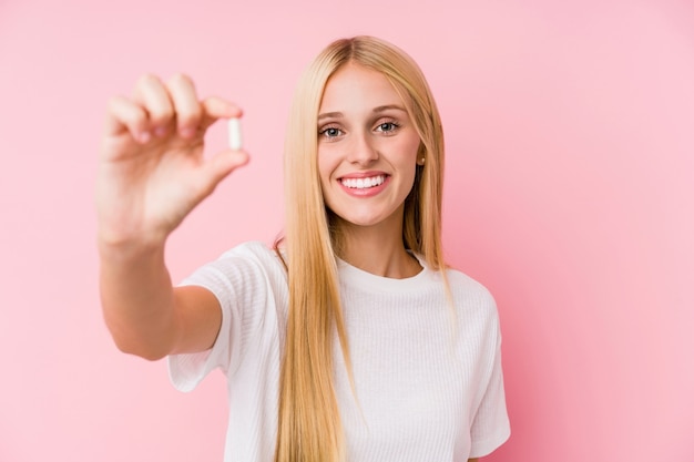 Joven rubia tomando unas pastillas aisladas en una pared.