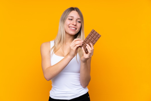 Joven rubia tomando una tableta de chocolate y feliz