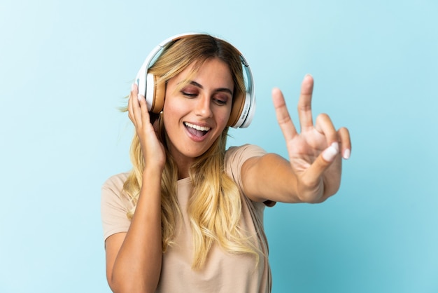 Joven rubia uruguaya aislada en azul escuchando música y cantando