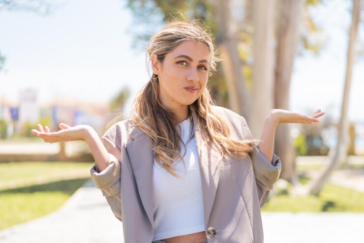 Foto una joven rubia uruguaya al aire libre con dudas mientras levanta las manos.