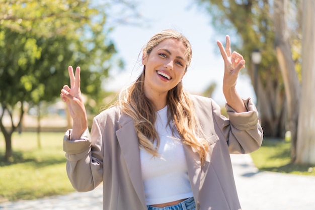 Foto una joven rubia uruguaya al aire libre mostrando el signo de la victoria con ambas manos