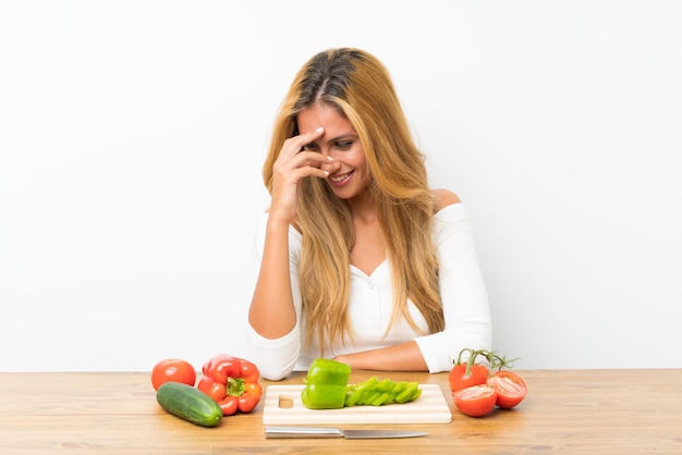 Joven rubia con verduras en una mesa riendo