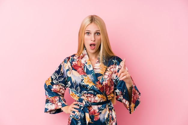 Joven rubia vestida con un pijama kimono teniendo una idea, concepto de inspiración.