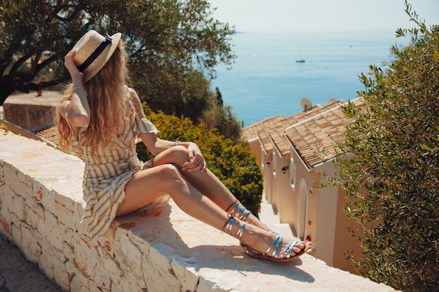 Joven rubia en vestido de verano mirando al mar turquesa