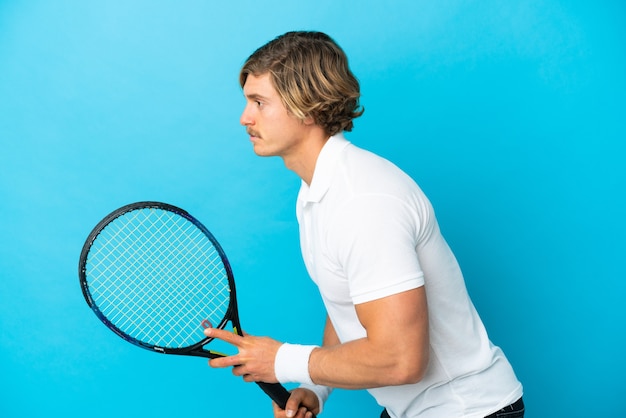 Joven rubio aislado en azul jugando al tenis