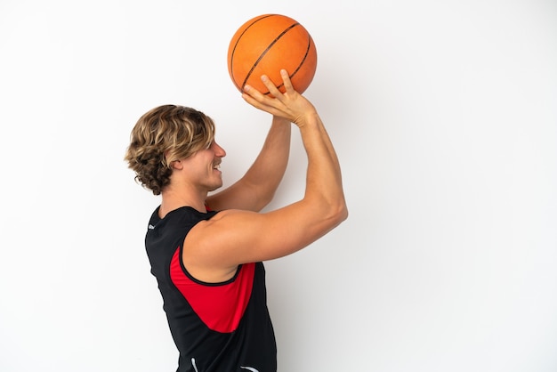 Joven rubio aislado en la pared blanca jugando baloncesto