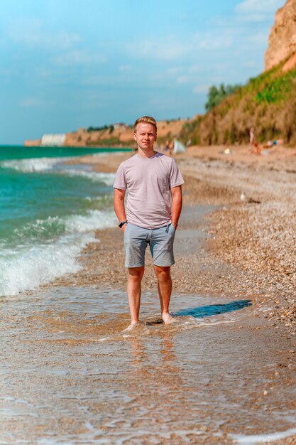 Un joven rubio camina por la playa cerca del océano azul o el mar El concepto de un verano feliz