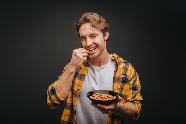 Joven rubio con camisa amarilla sostiene un plato de almendras y se lo come