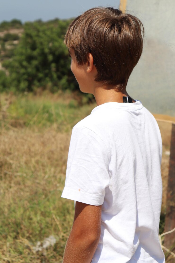 Joven rubio con camisa blanca y pantalones cortos azules disfrutando del sol de verano en la naturaleza