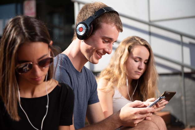 Joven rubio caucásico con auriculares y sonriendo mientras conversa rodeado de dos chicas