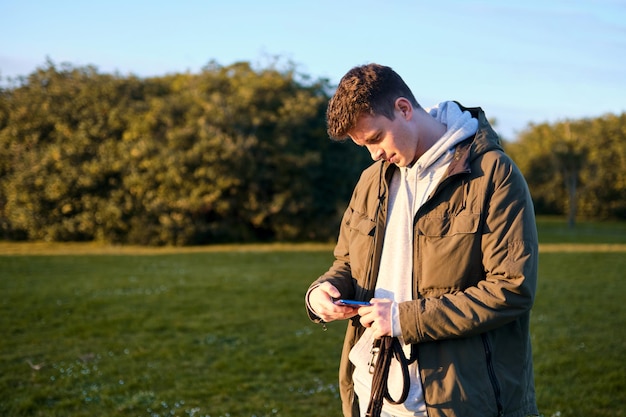 Joven rubio mirando con interés y extrañeza la pantalla de su teléfono móvil en un parque