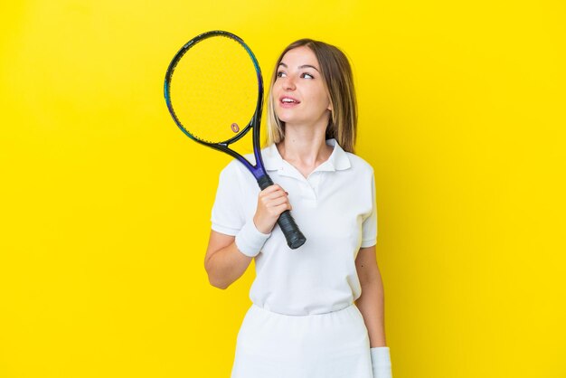 Joven rumana aislada sobre fondo amarillo jugando al tenis y mirando hacia arriba