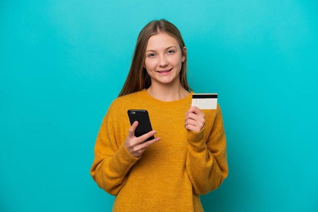 Joven rusa aislada de fondo azul comprando con el móvil con tarjeta de crédito