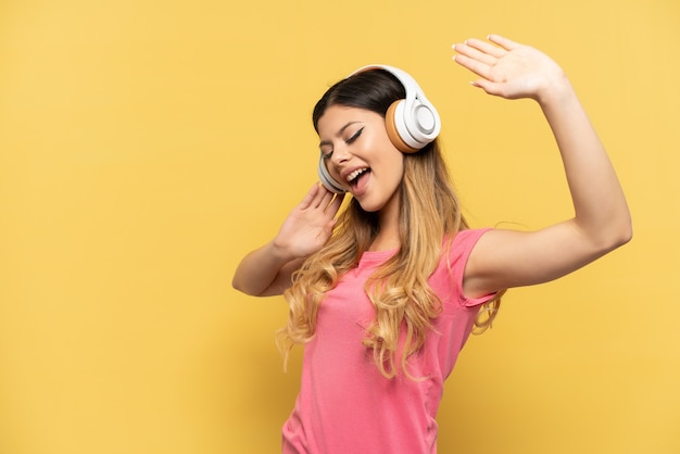 Joven rusa aislada sobre fondo amarillo escuchando música y cantando