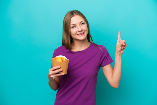 Joven rusa atrapando papas fritas aisladas de fondo azul mostrando y levantando un dedo en señal de lo mejor