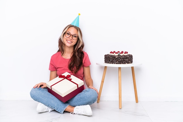 Joven rusa celebrando un cumpleaños sentada en el suelo aislada de fondo blanco con gafas y feliz