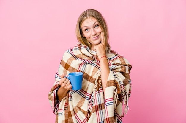 Joven rusa envuelta en una manta tomando café dudando entre dos opciones.
