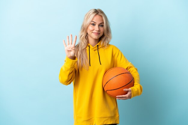 Joven rusa jugando baloncesto aislado en azul feliz y contando cuatro con los dedos