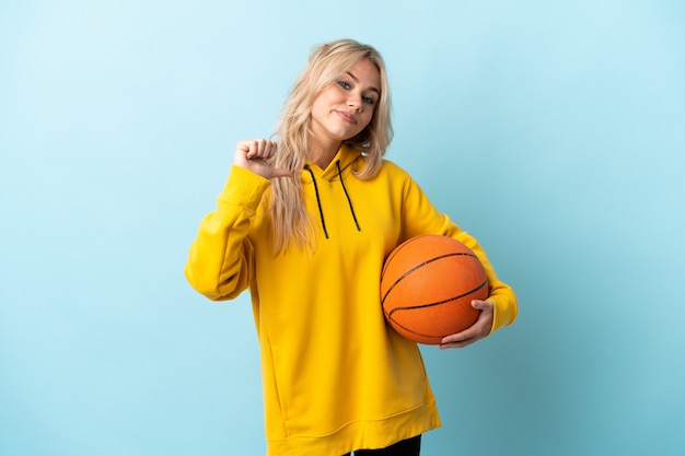 Joven rusa jugando baloncesto aislado en la pared azul orgulloso y satisfecho de sí mismo