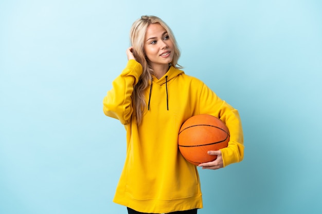 Joven rusa jugando baloncesto aislado en la pared azul pensando en una idea