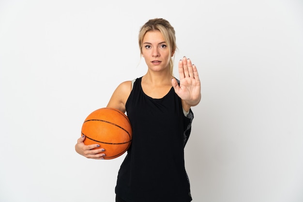 Joven rusa jugando baloncesto aislado en la pared blanca haciendo gesto de parada