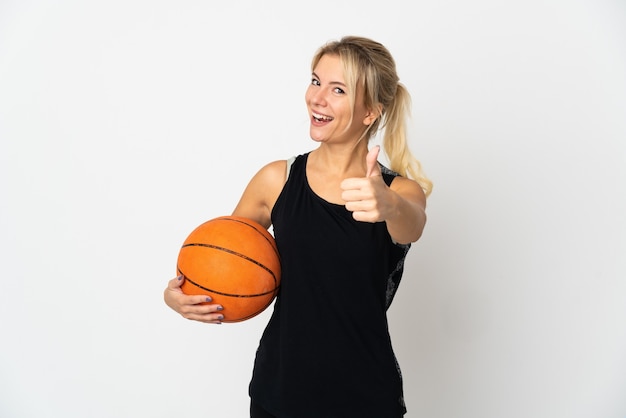 Joven rusa jugando baloncesto aislado en la pared blanca con los pulgares hacia arriba porque ha sucedido algo bueno