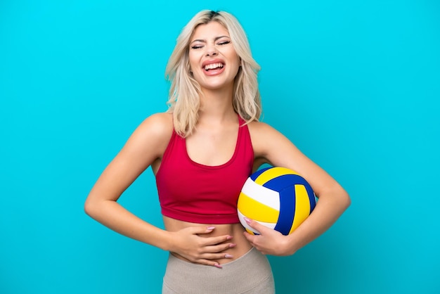 Joven rusa jugando voleibol aislada de fondo azul sonriendo mucho