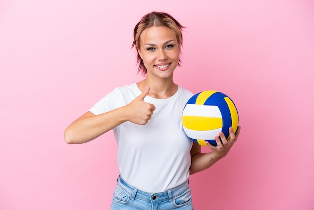 Joven rusa jugando voleibol aislado sobre fondo rosa dando un gesto de pulgar hacia arriba