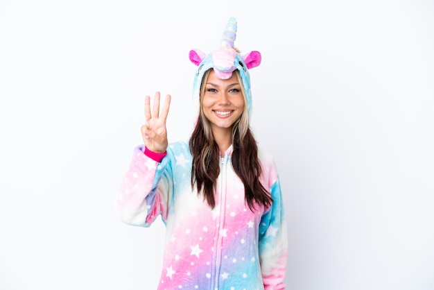 Joven rusa con un pijama de unicornio aislada de fondo blanco feliz y contando tres con los dedos