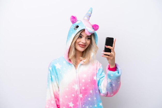 Joven rusa con pijama de unicornio aislada de fondo blanco haciendo un selfie