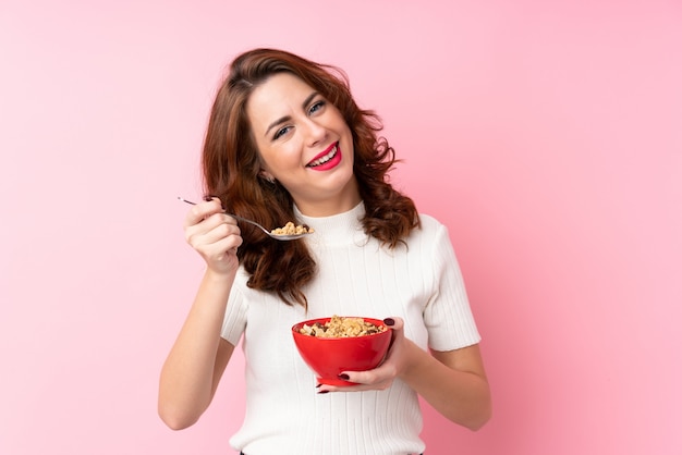 Joven rusa sobre rosa aislado sosteniendo un tazón de cereales