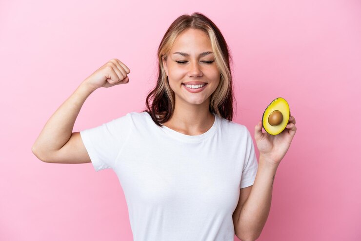 Foto joven rusa sosteniendo aguacate aislado de fondo rosa haciendo un gesto fuerte